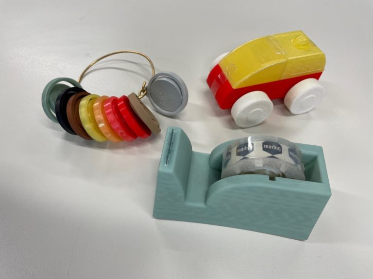 A toy car, a tape dispenser and a collection of round discs. All of the items have been made with 3D printing.